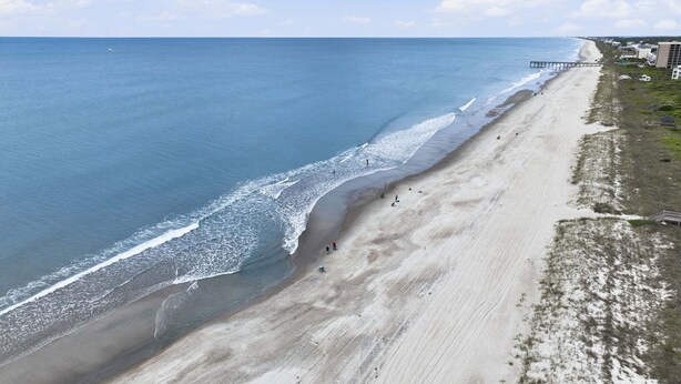 A beach with a pier extending into the ocean, a sandy shoreline, and buildings in the background. - Well-Appointed Condo with WiFi, Washer/Dryer & Shared Pools, Tennis (Atlantic Beach)