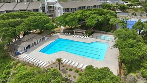 A swimming pool with lounge chairs, surrounded by trees and buildings, with a view of the sea. - Well-Appointed Condo with WiFi, Washer/Dryer & Shared Pools, Tennis (Atlantic Beach)