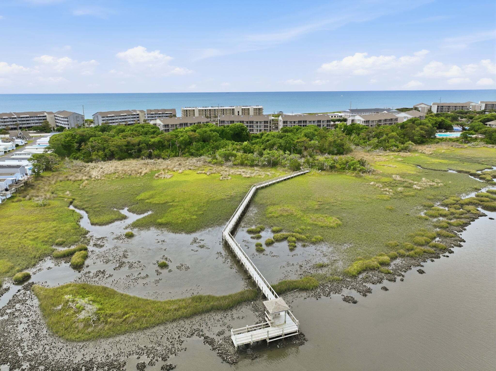 A coastal area with a bridge leading to a building complex, surrounded by greenery and water.