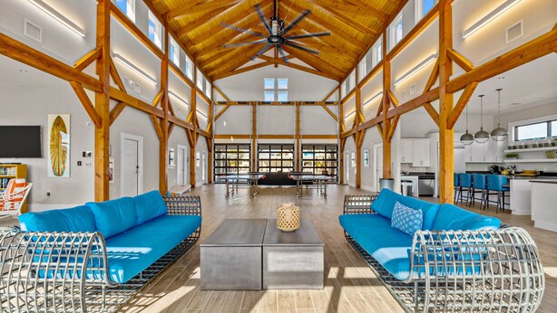 Un vaste espace intérieur doté de hauts plafonds, de poutres en bois et d’un coin salon central agrémenté de coussins bleus et de meubles en osier.