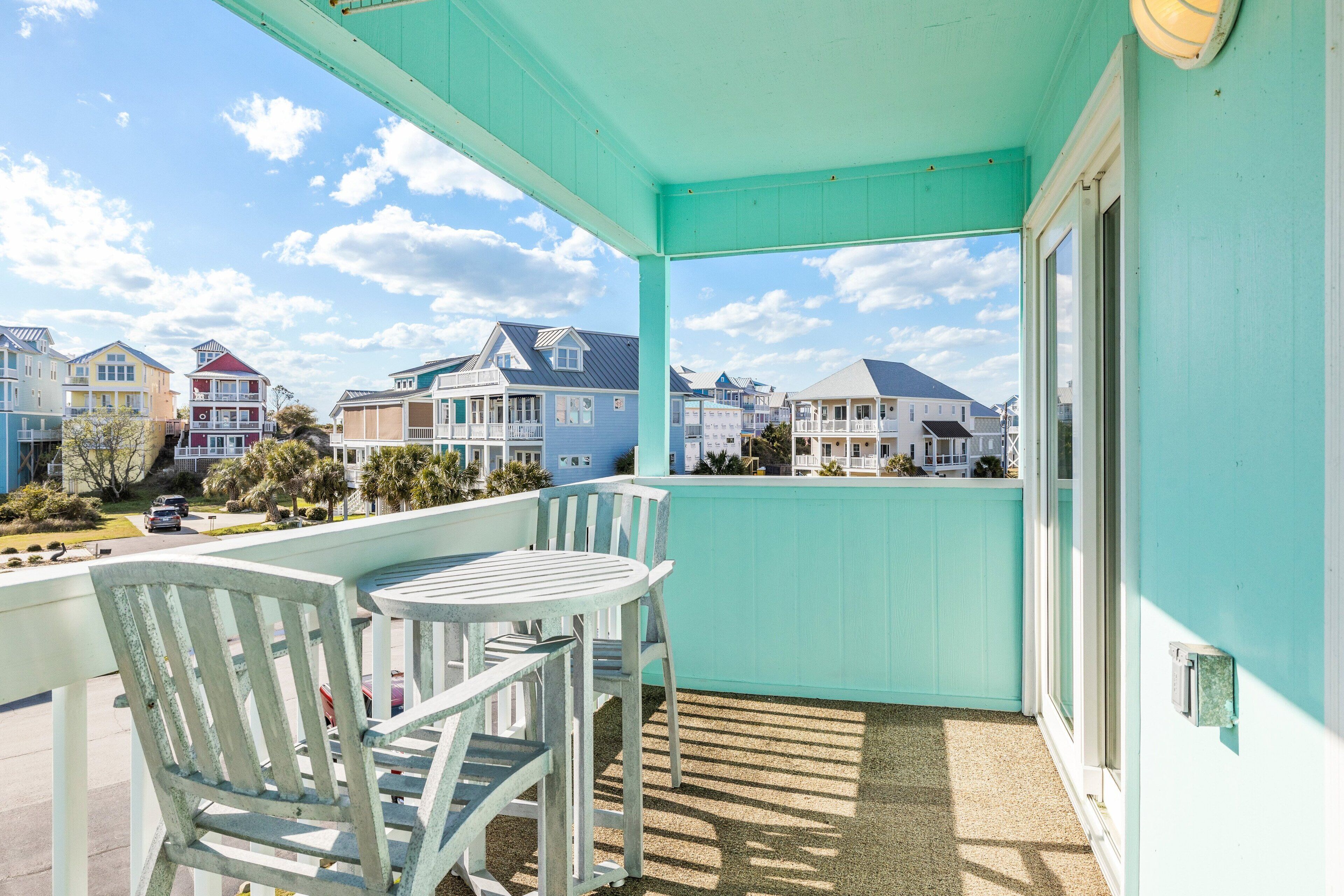 A balcony with a view of colorful houses, a table, and two chairs.