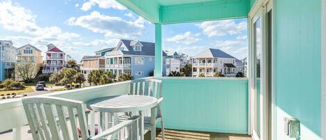 A balcony with a view of colorful houses, a table, and two chairs.