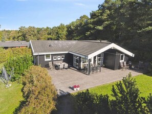 A two-story building with a covered patio area, a fenced garden, and a view of the surrounding forest. - 5 Star Holiday Home in Hojby (Hojby)