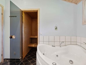 A bathroom with a wooden door, a white bathtub, and a tiled floor. - 5 Star Holiday Home in Hojby (Hojby)