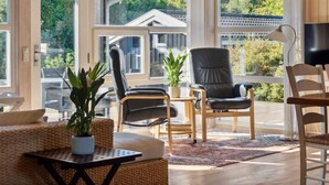 Una habitación amplia con ventanas grandes, un sillón de cuero negro, una mesa de madera y una planta en maceta.