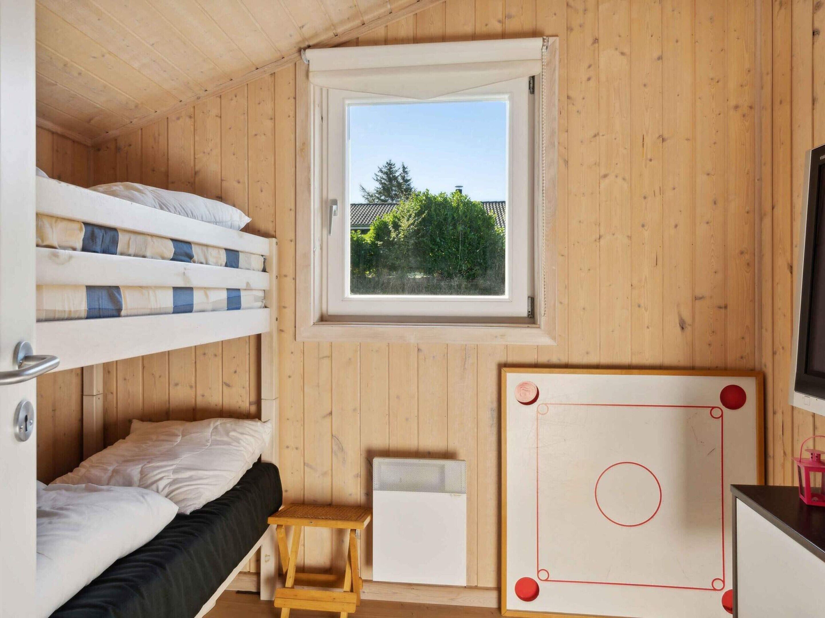 Une chambre avec un lit superposé, une fenêtre, une petite table et un tableau blanc.