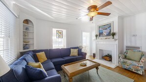 A living room with a sectional sofa, a wooden coffee table, a fireplace, and a ceiling fan. - Bullard Cottage: In the heart of Atlantic Beach w/ocean views (Atlantic Beach)