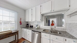 A kitchen with white cabinets, a granite countertop, a dishwasher, and a window with blinds. - Bullard Cottage: In the heart of Atlantic Beach w/ocean views (Atlantic Beach)
