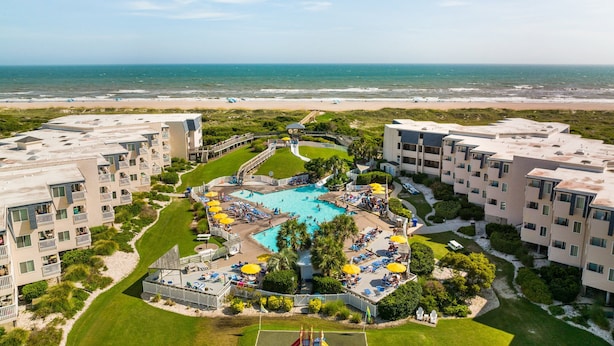 A resort with a central pool surrounded by multiple buildings, a beach view, and a well-maintained lawn. - Ocean view condo in beachfront complex with pools, tennis & beach gear (Atlantic Beach)