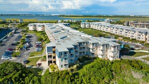 A multi-story hotel with balconies, a parking lot, and a view of the water. - Ocean view condo in beachfront complex with pools, tennis & beach gear (Atlantic Beach)