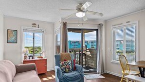 A living room with a sofa, a blue armchair, a wooden dining table, and a ceiling fan. - Ocean view condo in beachfront complex with pools, tennis & beach gear (Atlantic Beach)