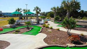A miniature golf course with green artificial turf, a winding path, and a few palm trees. - Ocean view condo in beachfront complex with pools, tennis & beach gear (Atlantic Beach)