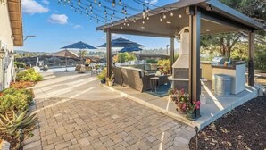 Un patio al aire libre con una parrilla, asientos y luces colgantes.