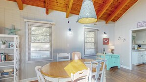 A dining area with a wooden table and white chairs, a hanging light fixture, and a white cabinet with a teal drawer. - 3rd-row beach cottage with ocean views, beach access, deck, & grill (Emerald Isle)