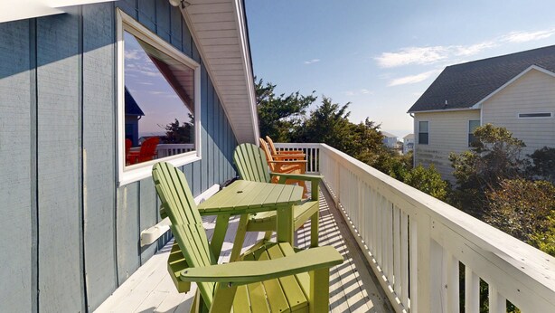 A balcony with green Adirondack chairs and a white railing. - 3rd-row beach cottage with ocean views, beach access, deck, & grill (Emerald Isle)
