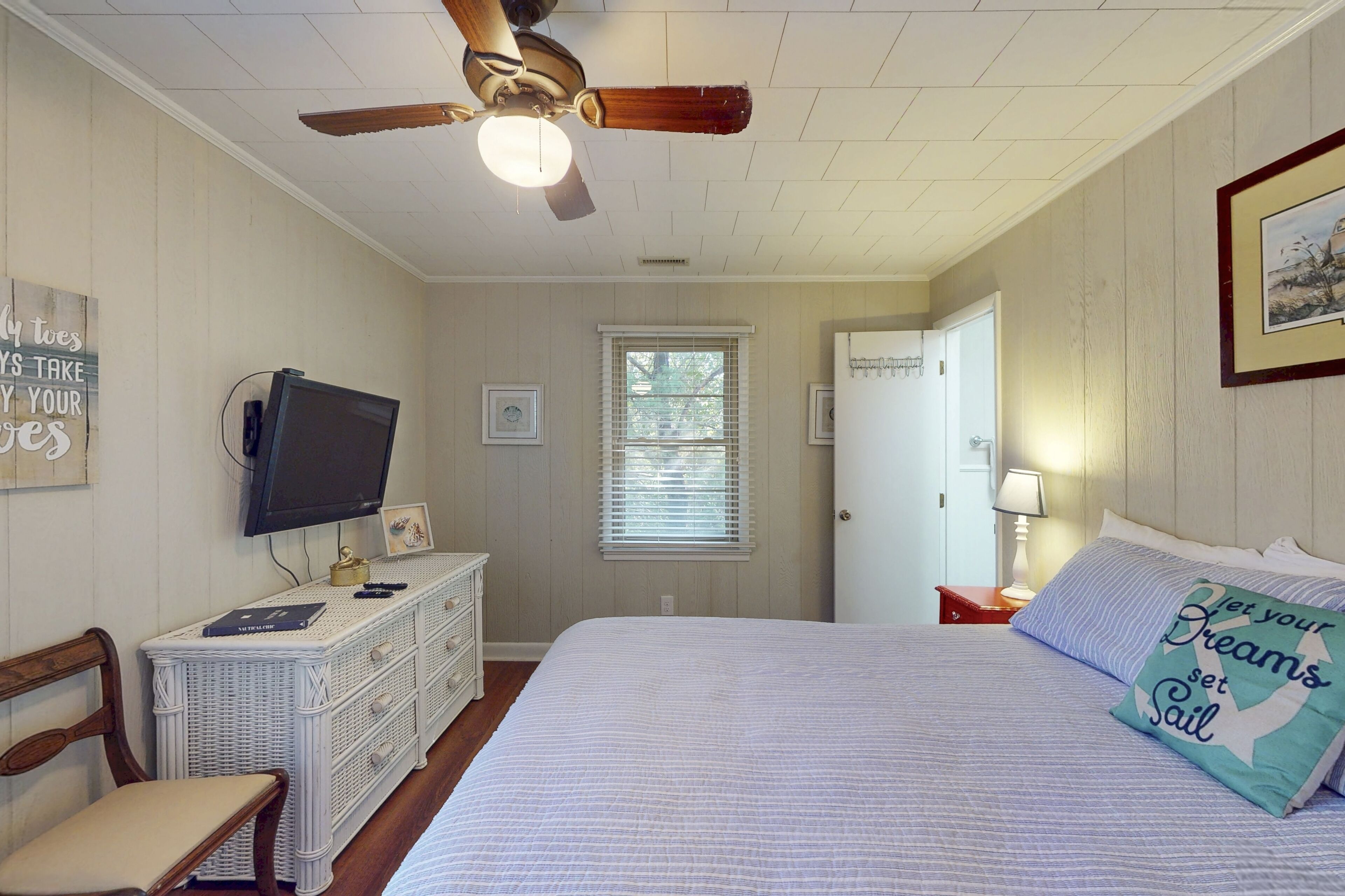 A bedroom with a bed, a ceiling fan, a dresser, a television, and a window.