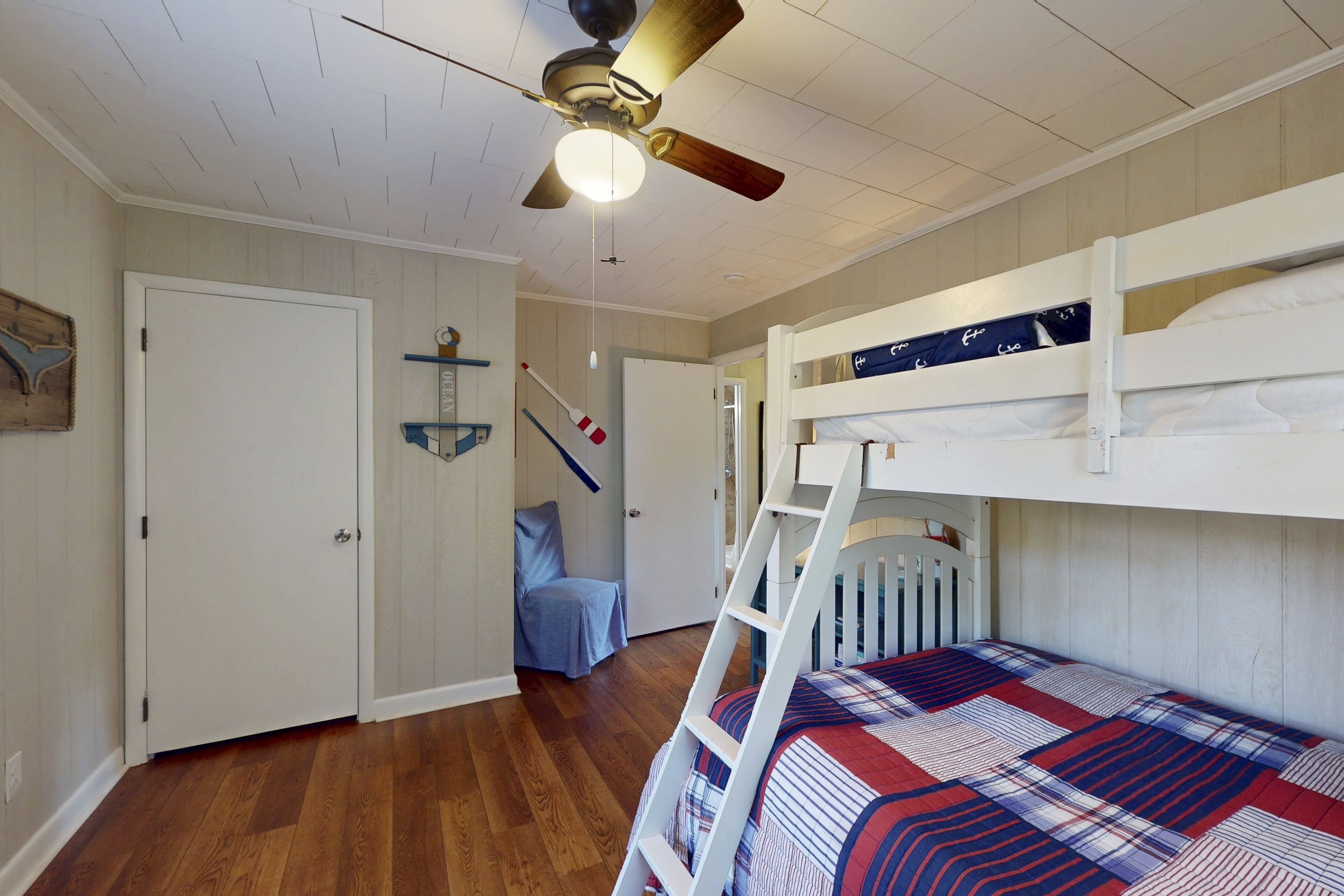 A bedroom with a bunk bed, wooden flooring, a ceiling fan, and a ladder.