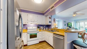 A modern kitchen with white cabinets, a stainless steel refrigerator, a built-in oven, and a dishwasher. - Bright Condo with WiFi, W/D, Screened Porch & Community Pool/Tennis/Day Dock (Atlantic Beach)