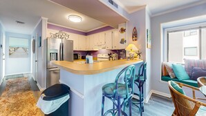 A kitchen with white cabinets, a built-in island with bar stools, and a window seat with cushions. - Bright Condo with WiFi, W/D, Screened Porch & Community Pool/Tennis/Day Dock (Atlantic Beach)