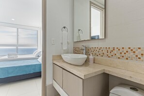 Ein modernes Badezimmer mit einem großen Spiegel, einem weißen Waschbecken und Meerblick durch das Fenster.