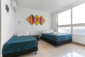 Habitación de hotel con dos camas, un ventanal grande y una decoración colorida en la pared.