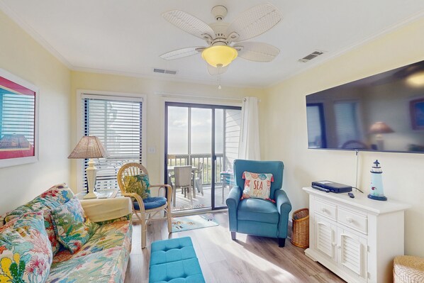 A living room with a ceiling fan, a sofa, a chair, a television, and a view through a glass door. - 3rd-Floor Condo in Oceanfront Building w/Ocean Views, Shared Pool, Free WiFi (Atlantic Beach)