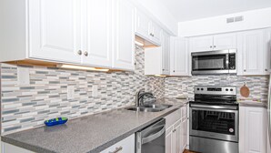 A modern kitchen with white cabinets, a stainless steel microwave, an oven, and a dishwasher. - Multi-Level, Oceanfront Condo in Pine Knoll Shores w/Free WiFi, Shared Pool (Pine Knoll Shores)