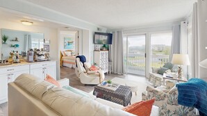 Un salón espacioso con un sofá, un sillón y una mesa de centro. Hay un televisor montado en la pared y un balcón con vistas.