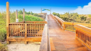 Un paseo marítimo de madera que conduce a una zona de playa, con un cartel que indica un aparcamiento.