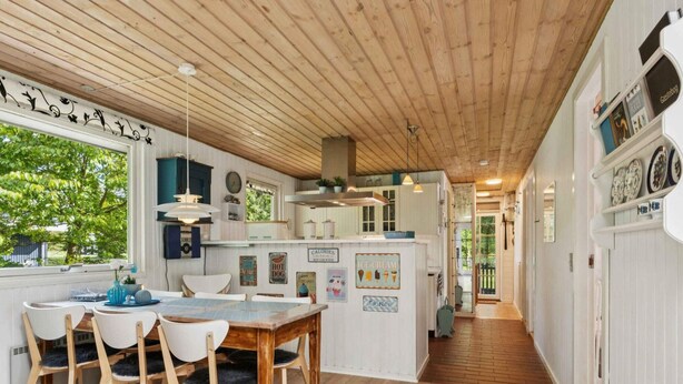 A kitchen with wooden floors, white cabinetry, and a dining area with chairs and a table. - 4 Star Holiday Home in Hadsund (Hadsund)