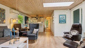 A spacious living area with a wooden floor, a sofa, a coffee table, and a chair. There is a kitchen visible in the background. - 4 Star Holiday Home in Hadsund (Hadsund)