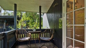 A covered porch with two wicker chairs and a small table, wooden deck, and a sliding glass door. - 4 Star Holiday Home in Hadsund (Hadsund)