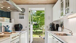 A kitchen with white cabinets, a stove, a sink, and a coffee maker. - 4 Star Holiday Home in Hadsund (Hadsund)