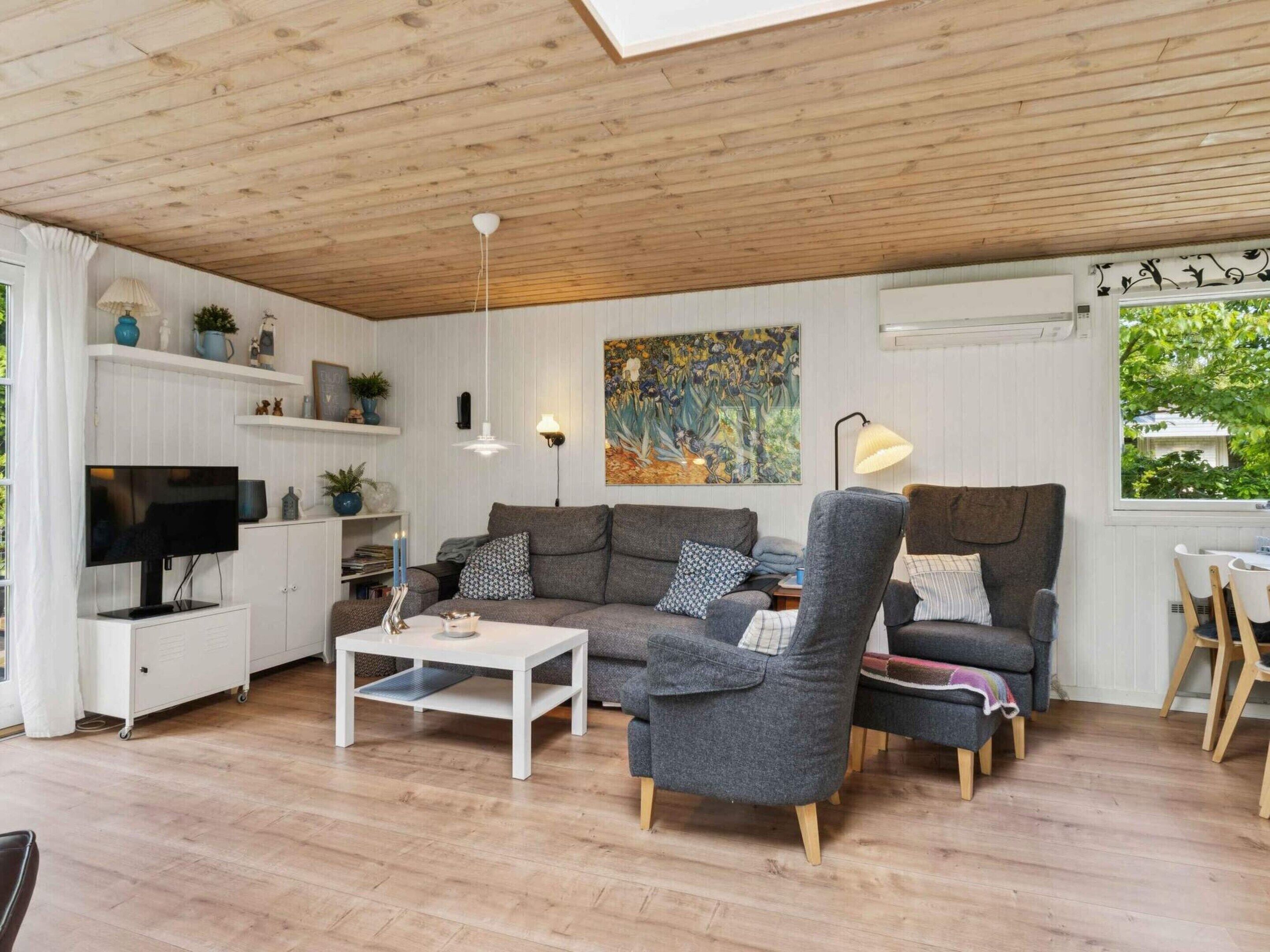 A cozy living room with a wooden ceiling, a flat-screen TV, a white coffee table, and grey sofas.