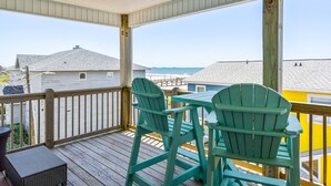 A covered deck with wooden railings, a table, and two green Adirondack chairs. - Ocean Crystal A: 2nd-row duplex, ocean views, walk to beach/pier (Atlantic Beach)