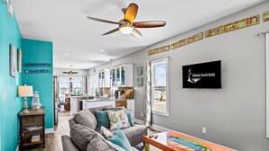 A modern living room with a grey sofa, teal walls, and a ceiling fan. - Ocean Crystal A: 2nd-row duplex, ocean views, walk to beach/pier (Atlantic Beach)