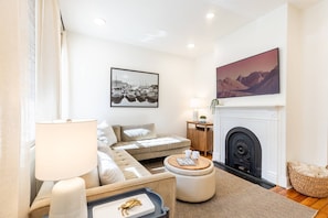 A living room with a sofa, a coffee table, a fireplace, and a painting on the wall.