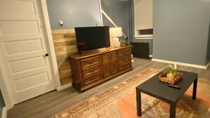 Una sala de estar con un aparador de madera, televisor, lámpara y una mesita con un control remoto.