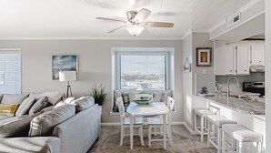 A modern kitchen with white cabinetry, a dining area with a table and chairs, and a ceiling fan.