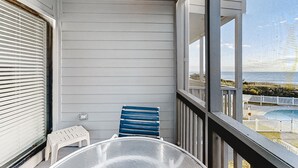 A balcony with a view of the ocean, a blue chair, a white table, and a small white stool.