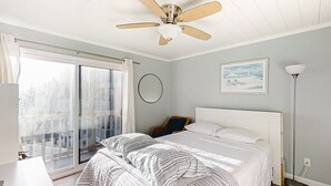 A bedroom with a bed, a ceiling fan, a large window with curtains, a floor lamp, and a painting on the wall.