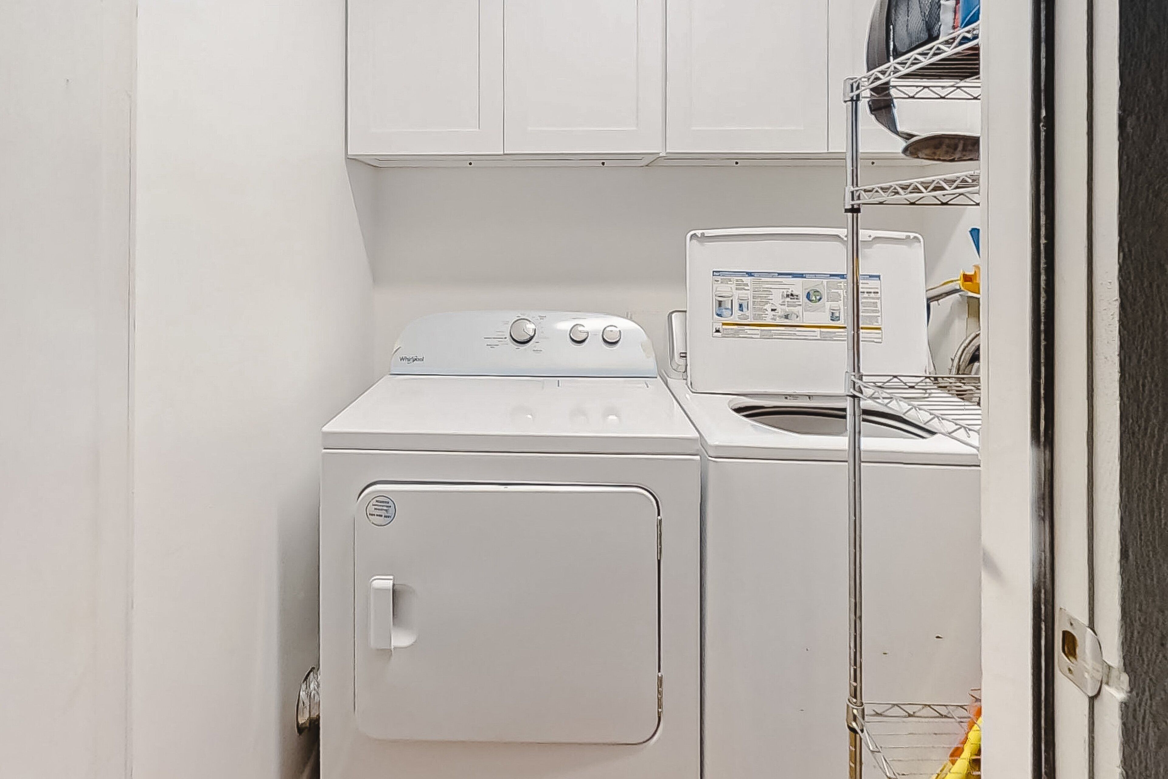 Un espace buanderie compact comprenant un lave-linge et un sèche-linge à chargement frontal, des étagères métalliques au-dessus et une porte donnant sur une autre pièce.