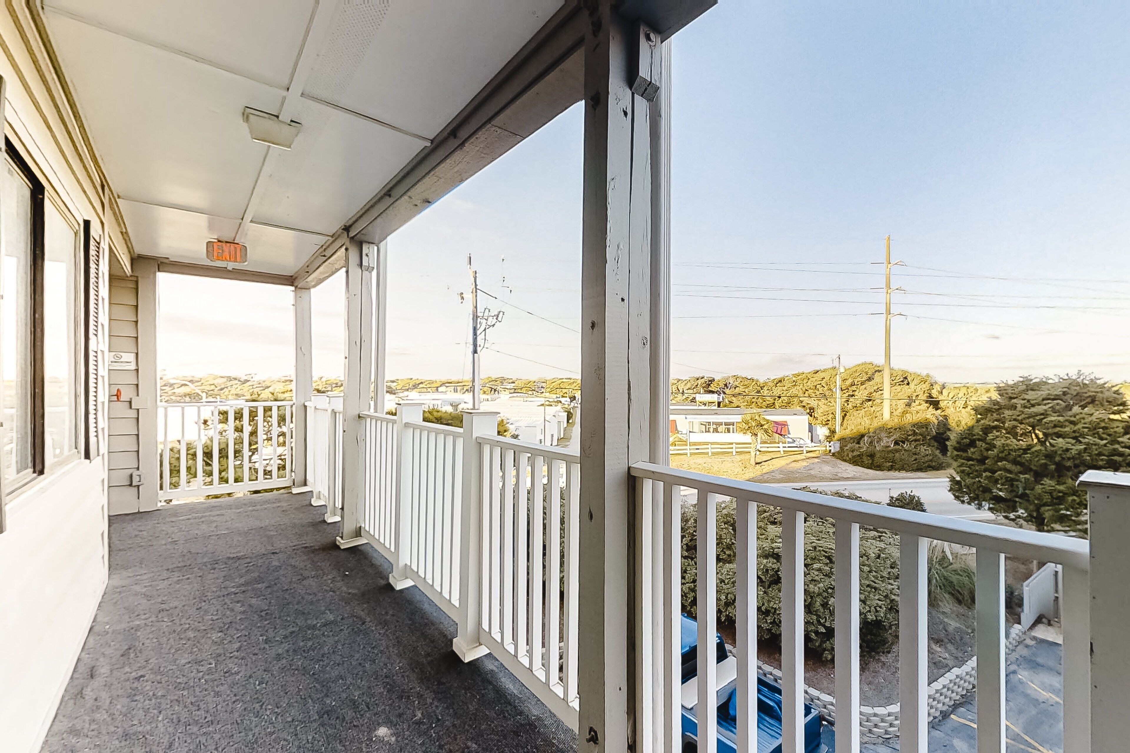 A covered balcony with white railings, a clear view of the surrounding area, and a sign indicating an exit.