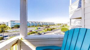 A balcony with a blue chair, overlooking a parking lot and buildings. - Second-Floor, Side Condo with Ocean View, WiFi & Shared Pools/Hot Tub/Tennis (Atlantic Beach)