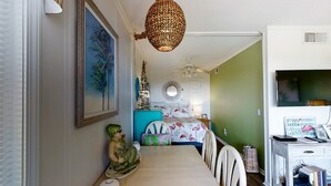 A dining area with a table, chairs, a decorative sculpture, a ceiling fan, and a television on a stand. - Second-Floor, Side Condo with Ocean View, WiFi & Shared Pools/Hot Tub/Tennis (Atlantic Beach)