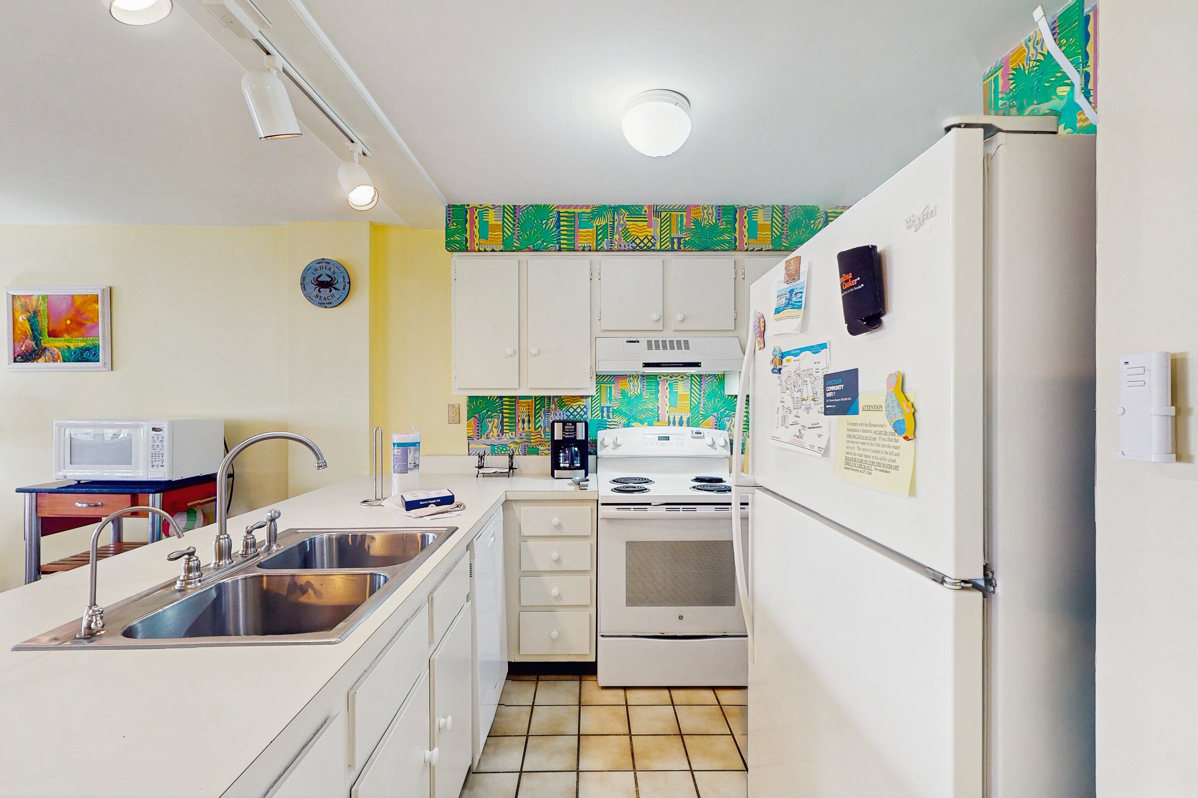 A compact kitchen with white appliances, a microwave, stainless steel sink, and a tiled backsplash.