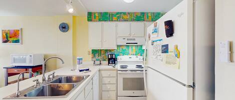 A compact kitchen with white appliances, a microwave, stainless steel sink, and a tiled backsplash.