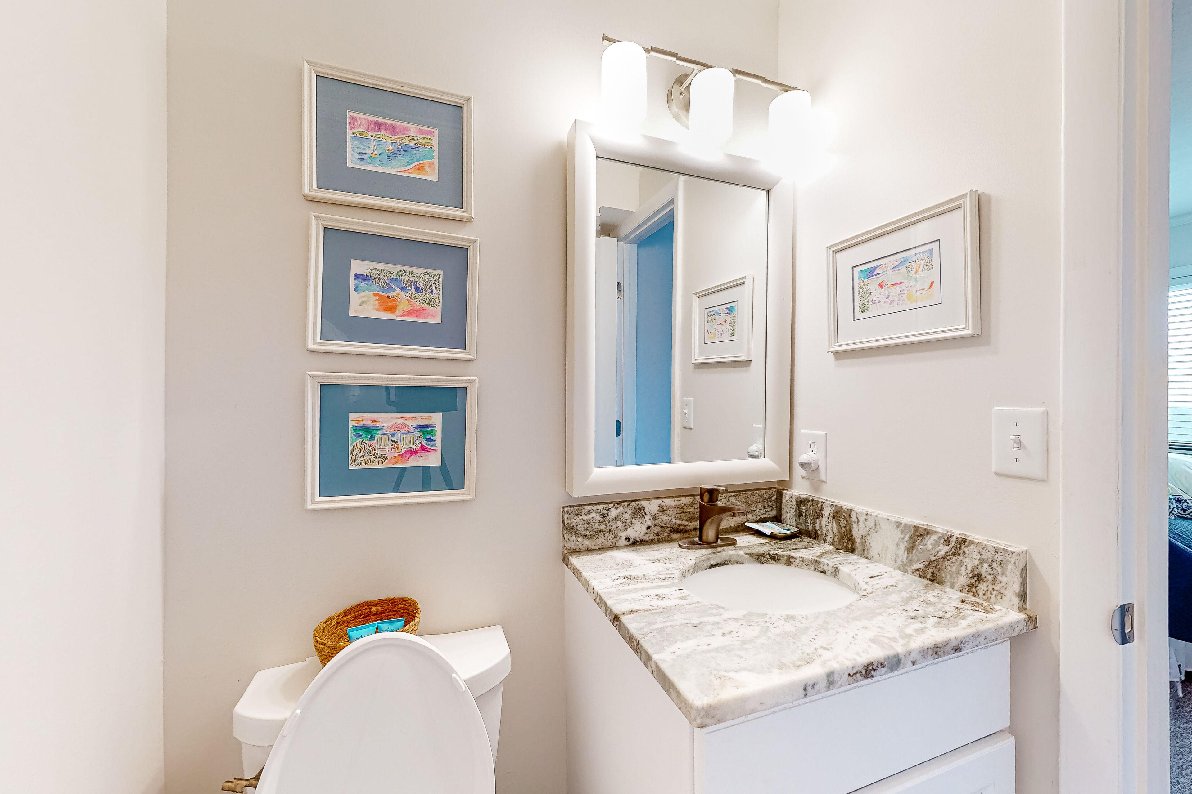 Een badkamer met een wit toilet, een marmeren wastafel en kunstwerken in een lijst aan de muur.