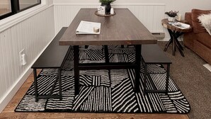 A dining area with a wooden table, black and white patterned rug, and a hanging light fixture. - Cozy Condo -Walk to Downtown McCall & Marina! Hot Tub, Indoor Pool, Sauna &more. (McCall)