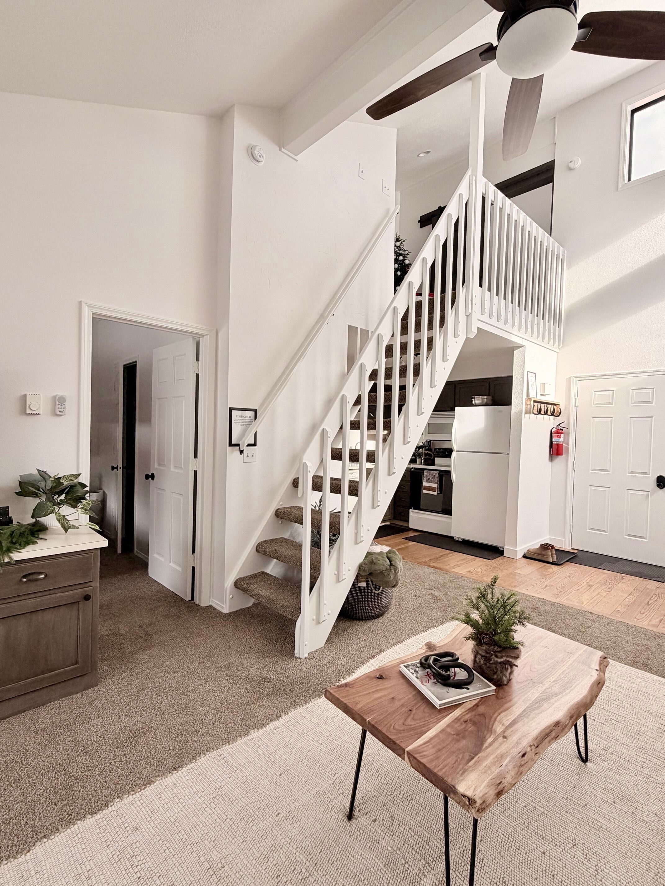 A spacious living area with a white staircase, a wooden coffee table, and a kitchen in the background.